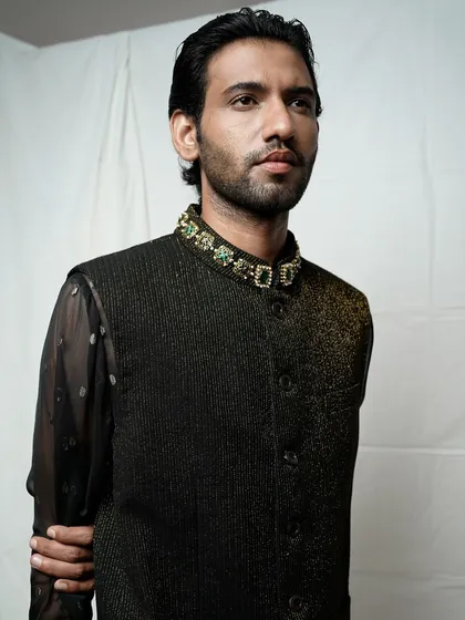 A close-up shot focusing on the details of a men's bandhgala jacket. The image highlights the textured fabric and the intricately jeweled collar, showcasing the luxury aspect of the garment.