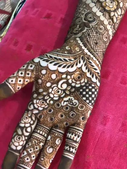 A close-up of a very detailed design, showing a mix of checkerboard, floral, and geometric fills. The white henna makes the patterns pop.