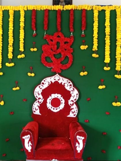 A traditional backdrop for a Half Saree ceremony with a green cloth background. The decor includes marigold garlands and a red floral Ganesha motif.
