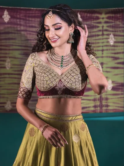 A smiling portrait of the model in the olive green lehenga, showcasing her elegant jewelry and the flattering fit of the custom-designed blouse.