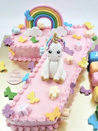 A first birthday is a huge milestone, and this number-shaped cake is a wonderful way to celebrate. This '1' cake is decorated in a unicorn theme with a rainbow, clouds, and colorful blocks spelling out the birthday girl's name.