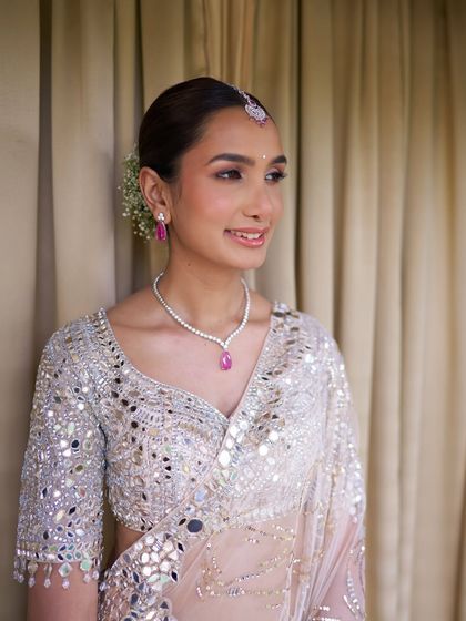 A serene portrait. The soft, peachy tones in her makeup complement her ivory lehenga and the warm, natural light.