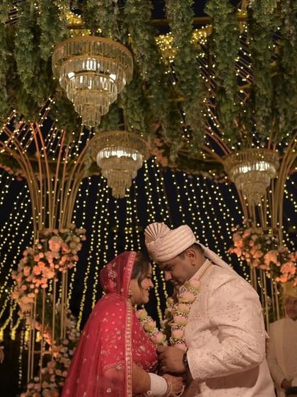 A sacred moment during the wedding ceremony, with the couple framed by the golden mandap structure, hanging chandeliers, and a sky of lights.