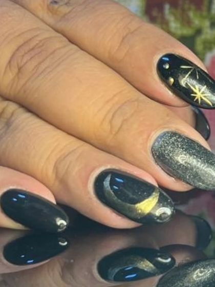 A celestial-themed manicure in black and grey, featuring gold moons, stars, and a shimmery cat-eye effect.