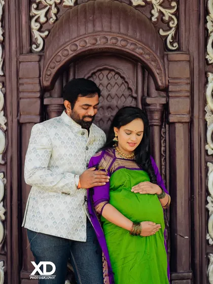 A tender moment as the partner gently holds the baby bump, both framed by an ornate wooden doorway.