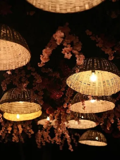 A ceiling of woven basket lamps and pink cherry blossoms creates a warm, intimate glow for an evening beach wedding celebration.