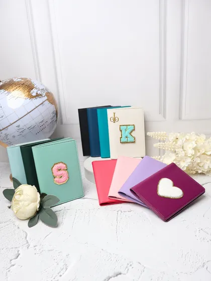 A display of our personalized passport covers in various colors like mint green, pink, and purple, customized with different chenille patches, including initials and a heart.