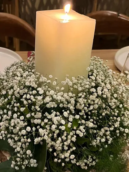 A simple yet beautiful centerpiece of a pillar candle nestled in a bed of baby's breath, creating a warm and intimate table setting.