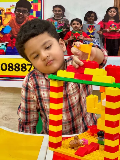 A young boy carefully places a flag on top of the tall, striped LEGO tower he is constructing.