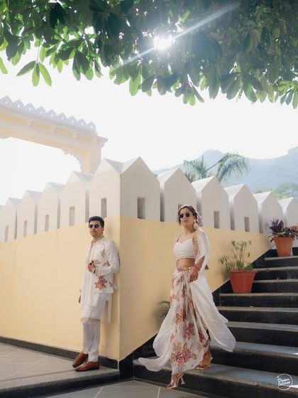 A stylish couple poses on the steps of their Udaipur wedding venue. The modern outfits contrast beautifully with the traditional architecture, showcasing a blend of contemporary style and timeless elegance.