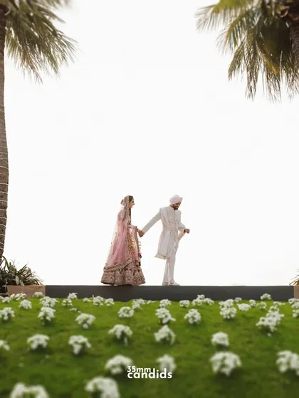 A creative, low-angle shot of the couple walking hand-in-hand, framed by palm trees. This perspective adds a unique and grand feel to their wedding portrait.