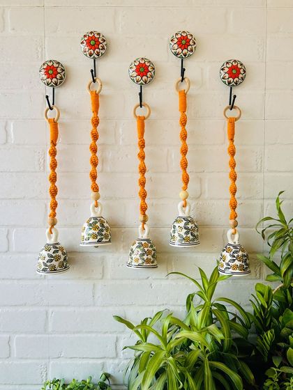 A set of five 'Blossom' macrame ceramic bells in a vibrant orange color. These handcrafted pieces are perfect for adding a pop of color and a touch of elegance to your garden or balcony.