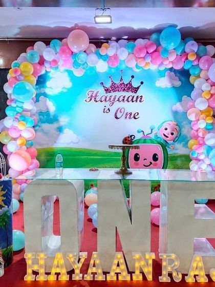 A pastel-colored Cocomelon theme for a first birthday. The setup includes a large 'ONE' table, character cutouts, and a soft-hued balloon arch.
