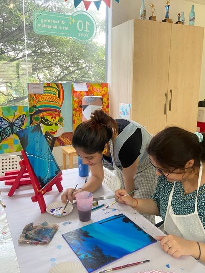 Two participants painting side-by-side in a canvas workshop. The studio provides a supportive and inspiring environment for all artists.