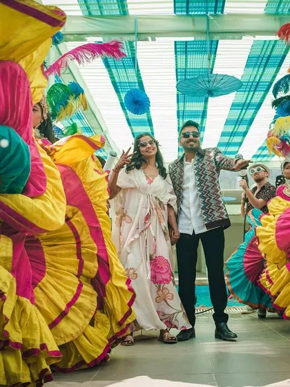 A beautiful shot of the couple during their pool party entry. They are framed by dancers in vibrant carnival costumes, creating a stunning photo opportunity.