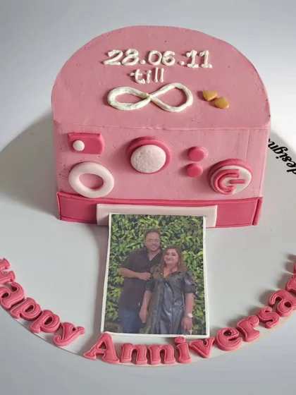 An anniversary cake designed as a pink Polaroid camera. The photo that slides out features a picture of the couple, making it a sweet and interactive gift.
