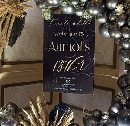 A stylish welcome area for an 18th birthday, featuring a black and gold balloon arch and a life sized cutout of the birthday boy.