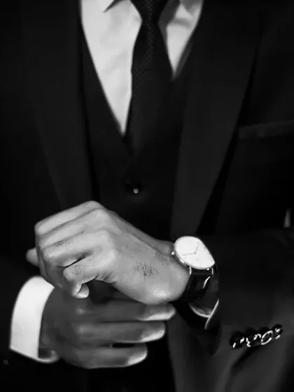 A groom's preparation is a story of quiet anticipation. This black and white detail shot focuses on the classic gesture of adjusting a cufflink and watch, highlighting the sharp lines of the suit and the timeless elegance of the moment.