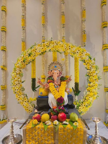 A circular arch of yellow and white flowers frames the Ganpati idol. The backdrop features hanging floral strings, adding depth and a traditional touch to this bright and cheerful setup.