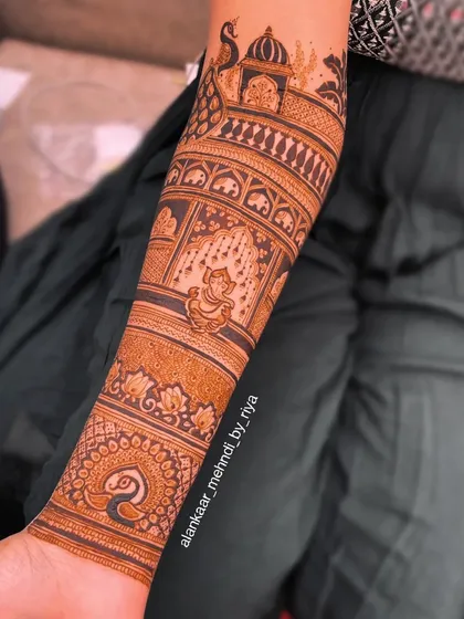 A beautiful bridal arm design featuring a depiction of the bride in a traditional swing (jhoola), surrounded by peacocks and palace art.