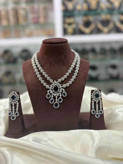 A double-layered AD necklace set with a central pendant. This versatile design comes in multiple colors including pink, white, emerald, and sapphire blue, making it a great addition to your inventory.