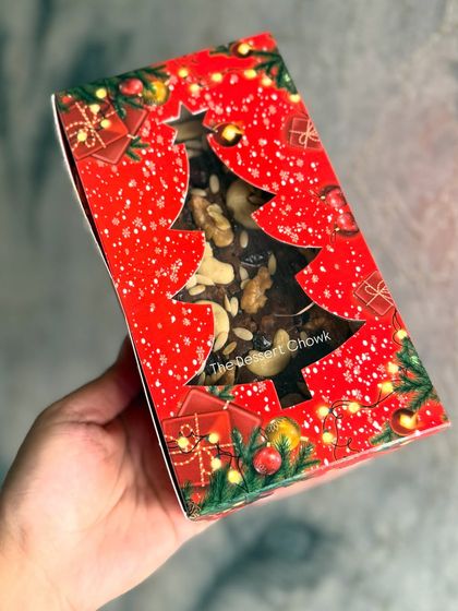 My eggless and no-alcohol Christmas Plum Cake in its festive packaging. The Christmas tree cutout gives a peek at the nut-filled cake inside.
