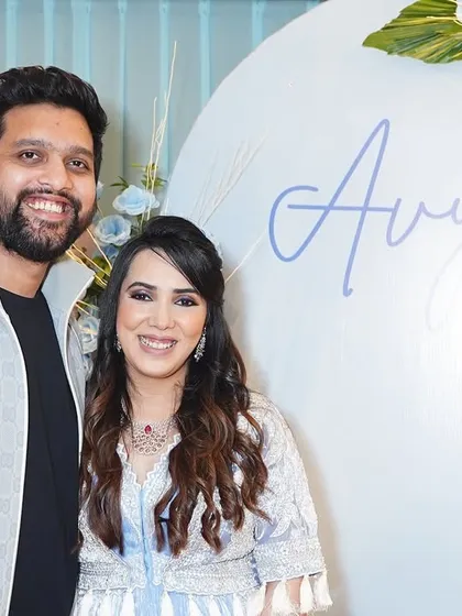 The happy parents posing in front of the custom backdrop we created. The personalized "Avyay" sign in a flowing script adds a beautiful, personal touch to the decor.