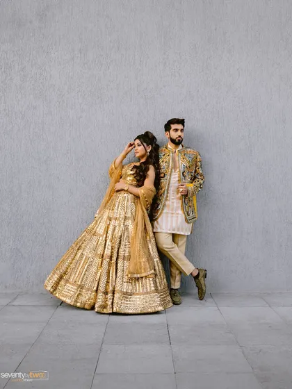 A full-length editorial portrait against a simple grey wall. Their stunning golden outfits pop, creating a high-fashion look that is both modern and regal.