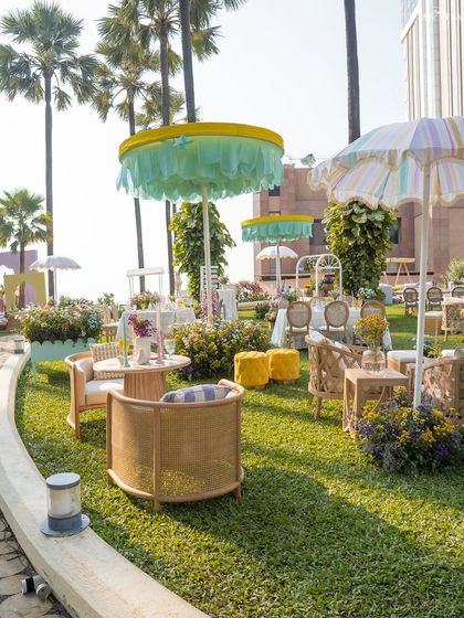 The lawn is filled with chic seating areas, featuring French cane furniture and custom-designed umbrellas in stripes and pastel shades.