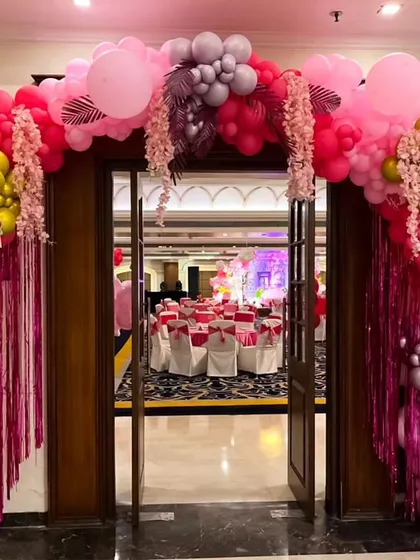 An elegant balloon arch is a classic way to frame the entrance to your event space. Here, I used a mix of pinks, reds, and metallic greys with floral and fringe accents to welcome guests into the banquet hall.