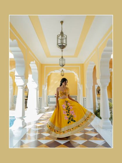 A vibrant bridal portrait in a sunlit palace corridor in Rajasthan. The bride's bright yellow lehenga and joyful twirl create a picture of pure happiness and celebration.