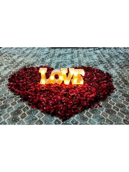 Another view of the "LOVE" marquee sign nestled in a heart of rose petals on the bed, a perfect centerpiece for your first night as a married couple.