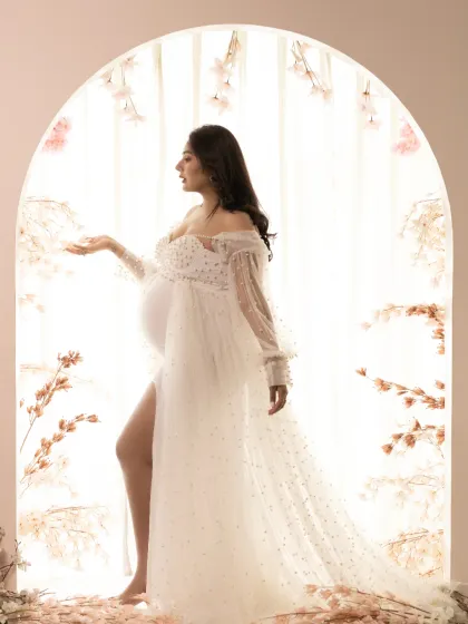 A divine and ethereal studio portrait. Backlit by a glowing arch, the mother-to-be is captured in a sheer, flowing gown, creating a silhouette that feels angelic and magical.