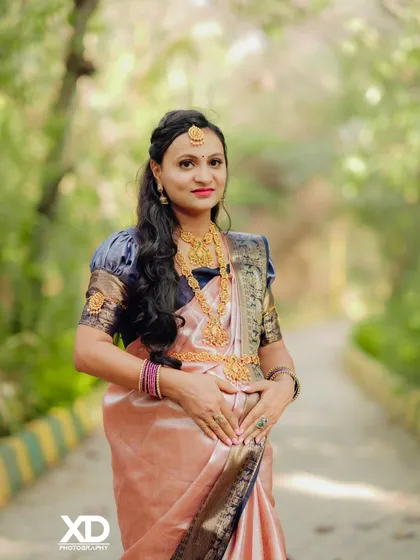 A beautiful solo portrait focusing on the mother-to-be, dressed in a stunning silk saree and traditional gold jewelry.