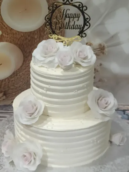 A pristine white two-tiered cake with delicate ridged buttercream and soft pink-tinted sugar roses. It’s a timeless design that brings a touch of class to any birthday.