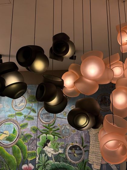 The Bocci 100 series seen at India Design 2025, with its mix of pink and grey pendants creating a sophisticated color palette against a painted mural.