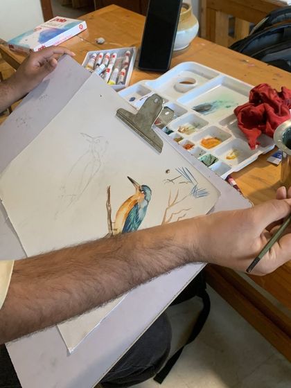 A student works on a watercolor painting of a kingfisher. Learning to paint birds requires a delicate touch and an understanding of feather textures, which we cover in our courses.