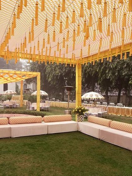 A wide view of the Haldi seating area, with long, comfortable divans for guests, set under a canopy decorated with yellow tassels.