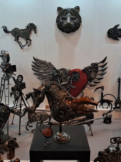 A collection of metal animal sculptures, including a tiger head and a winged creature, all made from recycled parts.