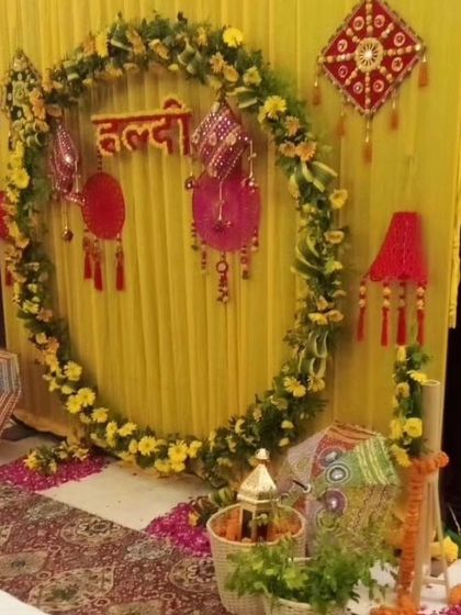 An indoor Haldi setup with a circular marigold backdrop and traditional Rajasthani hangings. The yellow fabric draping and patterned carpet complete the festive look.