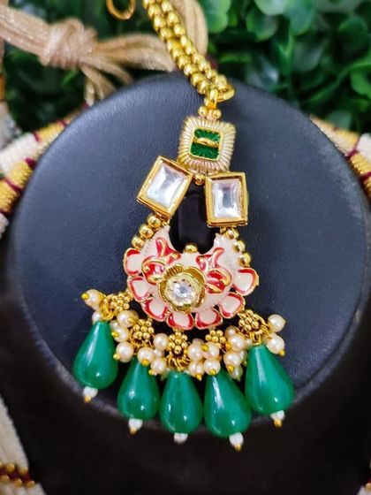 A close-up of a maang tikka with unique floral enamel work in red and white, accented with green beads. This piece is from my exclusive sale collection.