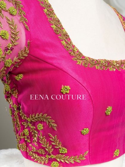 Grace in every detail. This pink net blouse features delicate leafy vines embroidered in gold and light green thread. The deep V-back and sheer sleeves add a touch of modern femininity.