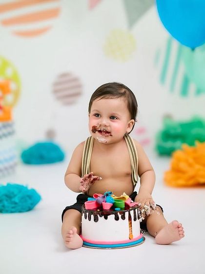 A vibrant and colorful cake smash setup. The bright decorations and chocolate-covered smile make this a truly fun and memorable first birthday photo.