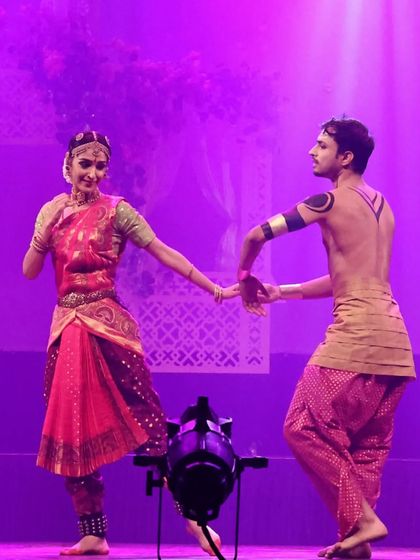 A scene from the production featuring a tender moment between two characters, illuminated by dramatic purple stage lighting. This highlights the theatrical storytelling aspect of the show.
