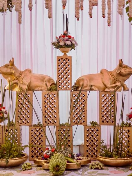 A decorative installation featuring golden cow statues on lattice stands, surrounded by brass elements and traditional flowers.