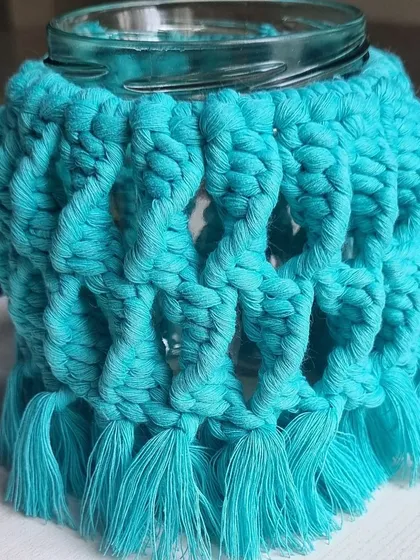 A close-up of a teal macrame jar cover, showing the intricate knots that create its unique texture.