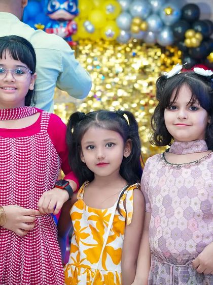 A group of young girls posing for a picture in front of a festive, sparkly gold backdrop at a party.