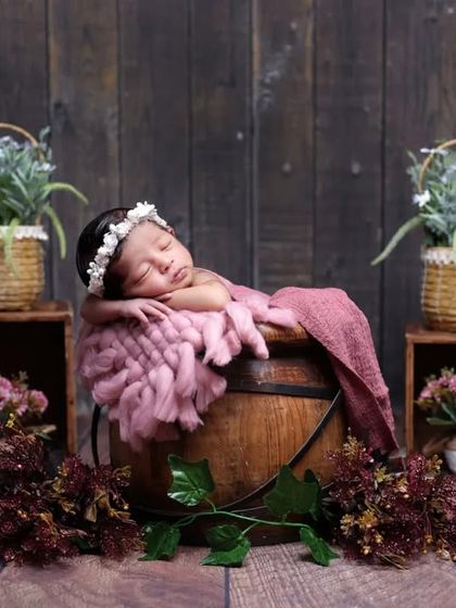 A rustic floral theme with the baby sleeping peacefully in a wooden bucket. The combination of the dark wood, pink fabric, and flowers creates a lovely contrast.