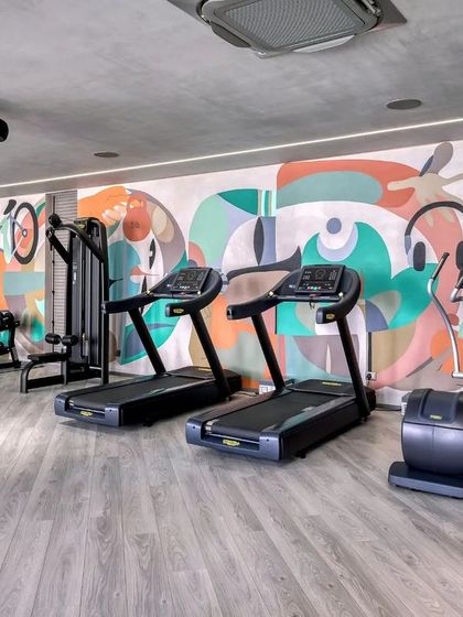 A vibrant, abstract mural designed for a gym clubhouse. The artwork incorporates dynamic shapes and figures related to fitness, like cycling and listening to music, to create an energetic and motivating environment.
