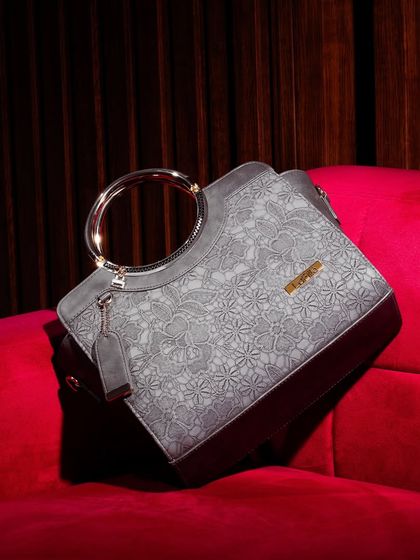 A luxury handbag with a unique floral texture and a metallic ring handle, placed on a rich, red velvet couch. This setting screams opulence and positions the product as a high-end statement piece.